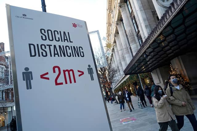 Pedestrians wearing a face mask or covering due to the COVID-19 pandemic, walk past a sign asking people to social distance, on Oxford Street in central London