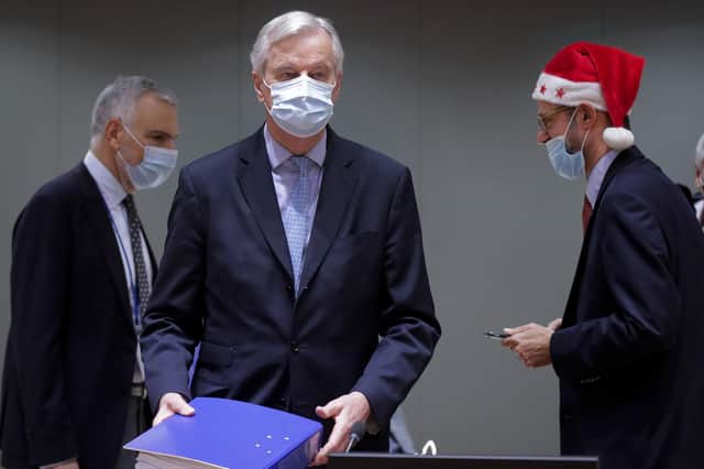 A collegue wears a Christmas hat as European Union chief negotiator Michel Barnier, centre, carries a binder of the Brexit trade deal during a special meeting of Coreper, at the European Council building in Brussels, Friday, Dec. 25