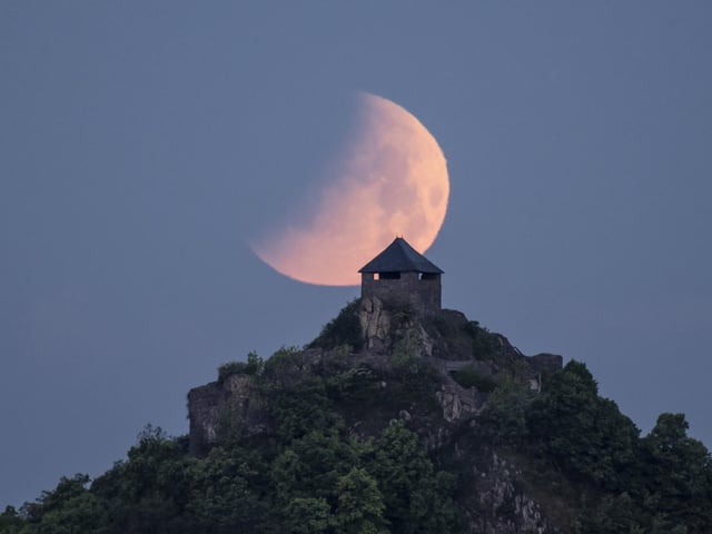 The moon during an eclipse above the Salgo Castle as viewed from Salgotarjan, Hungary, early Monday, May 16, 2022. (Peter Komka/MTI via AP)