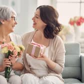 Happy mother's day! Beautiful young woman and her mother with flowers and gift box at home. Pic: Adobe