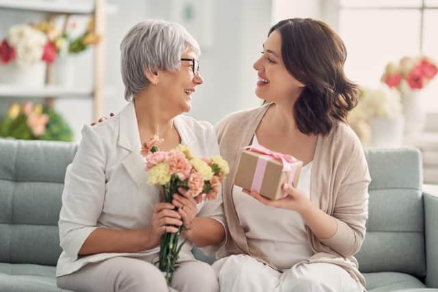 Happy mother's day! Beautiful young woman and her mother with flowers and gift box at home. Pic: Adobe