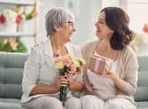 Happy mother's day! Beautiful young woman and her mother with flowers and gift box at home. Pic: Adobe