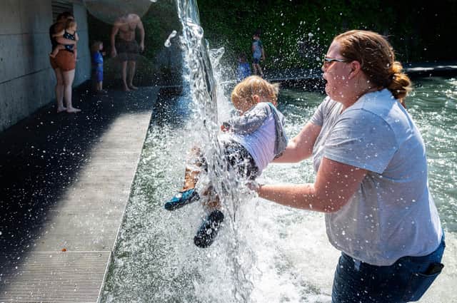 A woman holds a young child under a waterfall at a park in Washington, DC, during the recent heatwave that affected much of North America (Picture: Jim Watson/AFP via Getty Images)