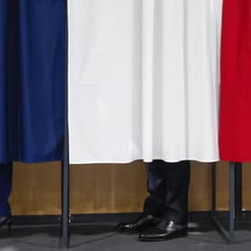 France's President Emmanuel Macron, flanked by his wife Brigitte Macron, in a polling booth, adorned with curtains displaying the colors of the flag of France (Pic: Mohammed Badra/Pool/ AFP)