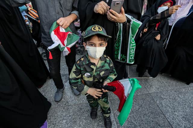 A young boy wearing military fatigues used by Iran's Revolutionary Guards stands holding a plastic gun and a national flag with a pin on his chest depicting the Guards' late commander Qasem Soleimani as supporters of Ebrahim Raisi celebrate his election victory (Picture: Atta Kenare/AFP via Getty Images)