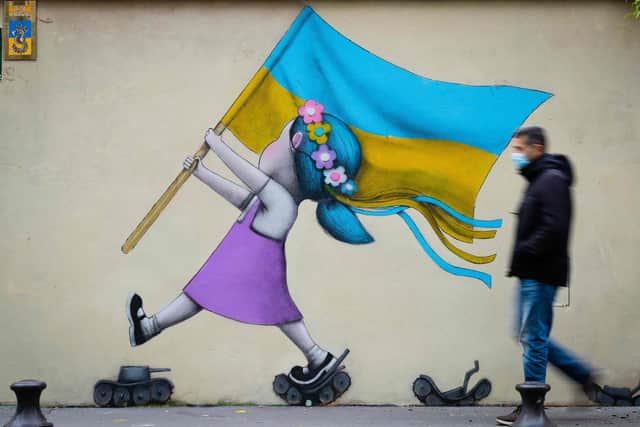 A bystander walks past a fresco by street artist Seth depicting a girl with a Ukrainian flag walking on tanks in Paris. Picture: Joel Saget/AFP via Getty Images