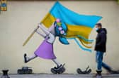 A bystander walks past a fresco by street artist Seth depicting a girl with a Ukrainian flag walking on tanks in Paris. Picture: Joel Saget/AFP via Getty Images