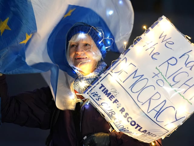 A person attends a rally outside the Scottish Parliament in Edinburgh with a sign reading "we have a right to democracy"