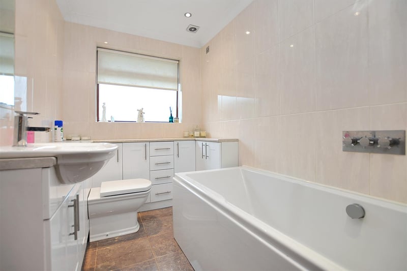Contemporary three piece suite, comprising a panelled bath with wall-mounted 'rain' shower, large vanity unit with inset basin and ample storage beneath and WC.