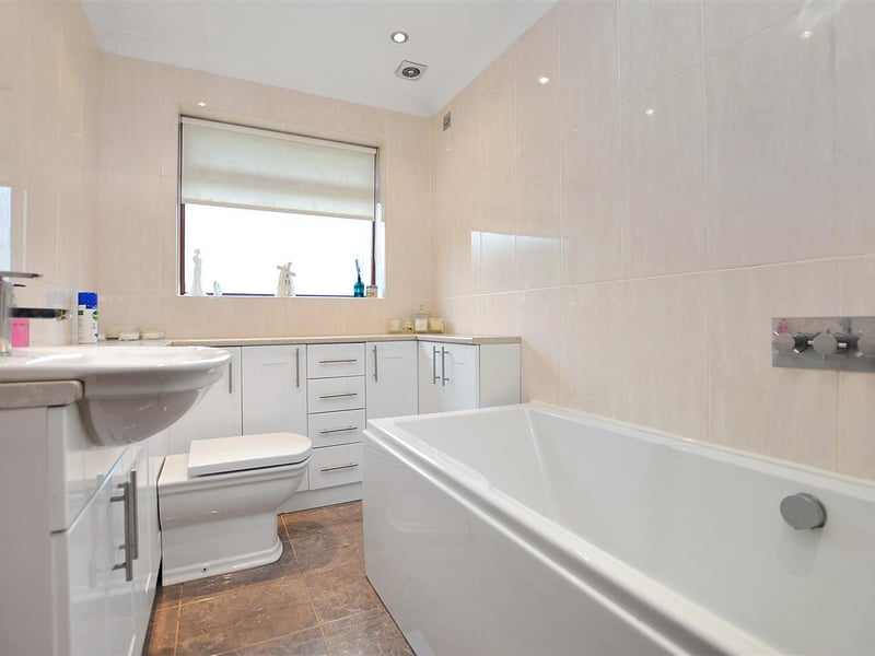 Contemporary three piece suite, comprising a panelled bath with wall-mounted 'rain' shower, large vanity unit with inset basin and ample storage beneath and WC.