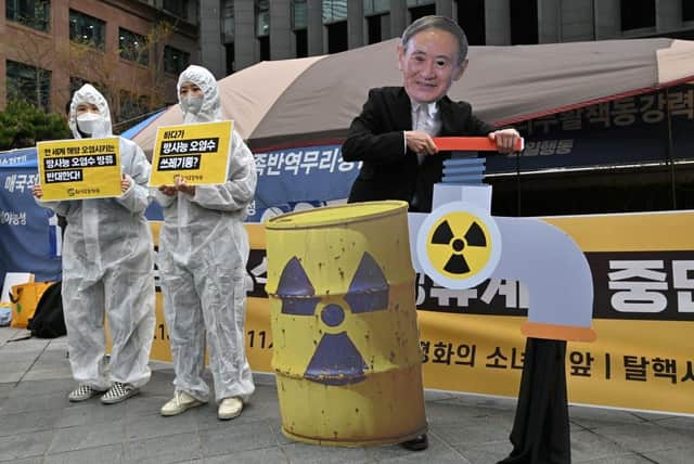 South Korean environmental activists wearing protective clothing and a mask of Japan's Prime Minister Yoshihide Suga perform during a protest against Japan's decision on releasing Fukushima wastewater, near the Japanese embassy in Seoul on April 13, 2021.