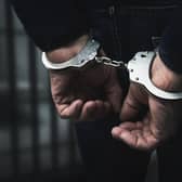 arrested man with cuffed hands behind prison bars