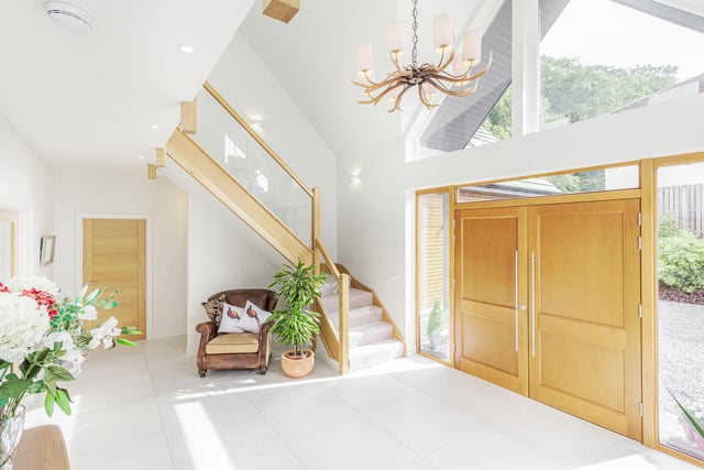 Interior: A double-height reception hall leads to a formal lounge, open-plan kitchen-dining area with French doors, and a vaulted family area with free-standing wood-burning stove. Upstairs, the ensuite principal bedroom has full-height windows and the fifth bedroom is used as a cinema.