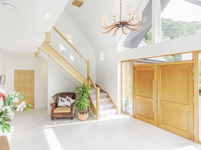 Interior: A double-height reception hall leads to a formal lounge, open-plan kitchen-dining area with French doors, and a vaulted family area with free-standing wood-burning stove. Upstairs, the ensuite principal bedroom has full-height windows and the fifth bedroom is used as a cinema.