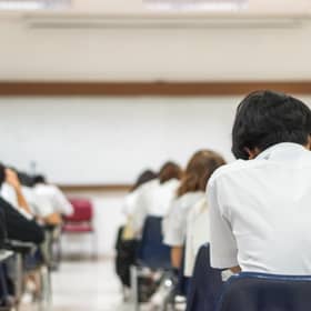School students writing answer doing exam in classroom