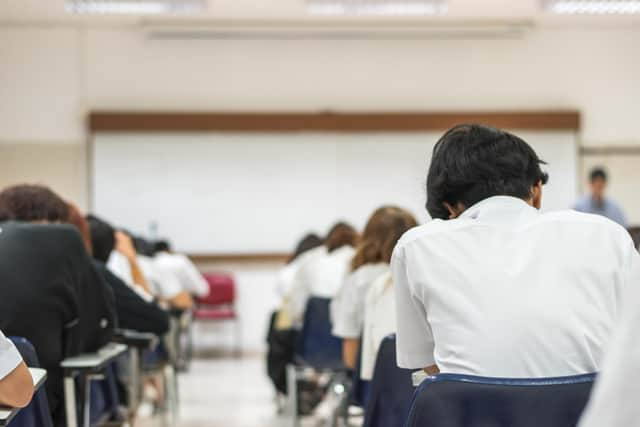 School students writing answer doing exam in classroom