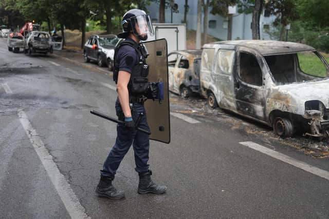 A French police officer in riot gear looks on next to burnt cars at the Pablo Picasso neighbourhood in Nanterre