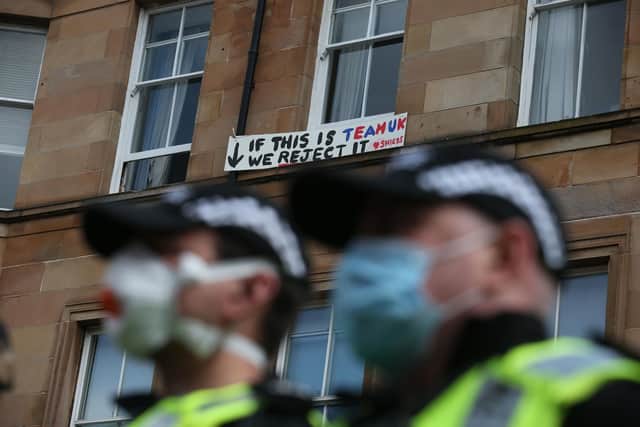 A man holds a sign out of a window above police guarding an immigration van in Kenmure Street, Glasgow which is surrounded by protesters.