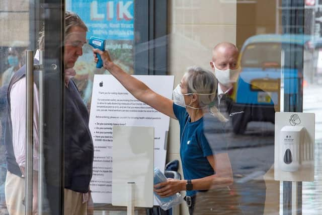 A retail worker wearing PPE takes the temperature of a customer entering the Apple Store on Princes Street in Edinburgh on June 29, 2020. (Photo by Lesley MARTIN / AFP) (Photo by LESLEY MARTIN/AFP via Getty Images)