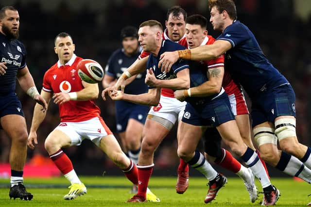 Scotland's Finn Russell (centre) is tackled by Wales' Josh Adams during the Guinness Six Nations match at the Principality Stadium, Cardiff. Picture date: Saturday February 3, 2024.