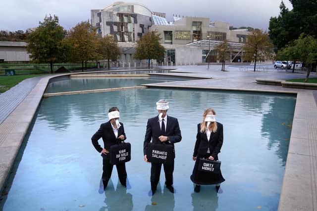 Suited performers from Ocean Rebellion, wearing blindfolds and gagged with dead fish, protest at Holyrood Pond, outside the Scottish Parliament in Edinburgh, calling on Scottish Government to wind down the environmental tragedy of salmon farming with a just transition for workers. Picture date: Friday October 7, 2022.