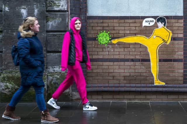 Members of the public walk past a piece of street art by 'Palley' that features Bruce Lee kicking a coronavirus molecule in Glasgow's East End.