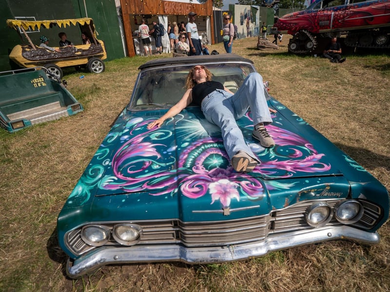 A person relaxes on the bonnet of a car at the Glastonbury Festival at Worthy Farm in Somerset.