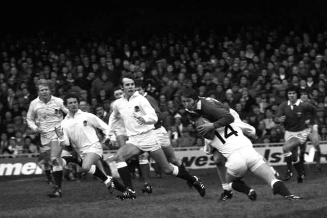 JPR Williams, with the ball, finds himself tackled by England's right wing John Carleton, as he tries to weave through a crowd of white jerseys at Cardiff Arms Park during the international match where Williams made a record 54th appearance.
