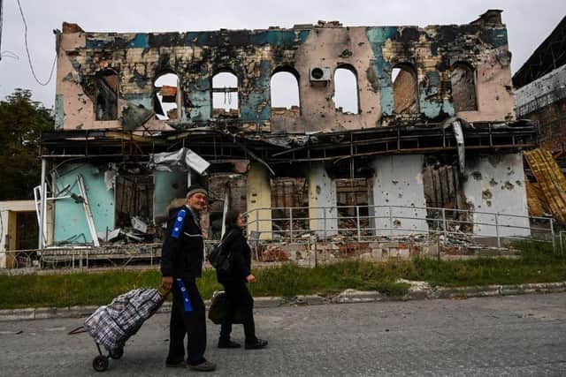 A couple wheel suitcases as they walk in front of a destroyed building in Izyum, Kharkiv Region, eastern Ukraine, amid the Russian invasion of Ukraine.