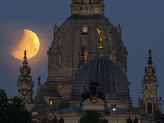 The moon sets in the morning during a partial lunar eclipse behind the Frauenkirche and the dome of the Kunstakedmie with the angel "Fama" in Dresden, Germany (Robert Michael/dpa via AP)