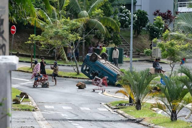People gather near an overturned car in the Motor Pool district in Noumea, New Caledonia, amid protests linked to a debate on a constitutional bill aimed at enlarging the electorate for upcoming elections of the overseas French territory.