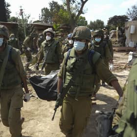 Israeli soldiers carry a body of a person killed in Hamas attack in kibbutz Kfar Azza. Photo: AP Photo/Erik Marmor