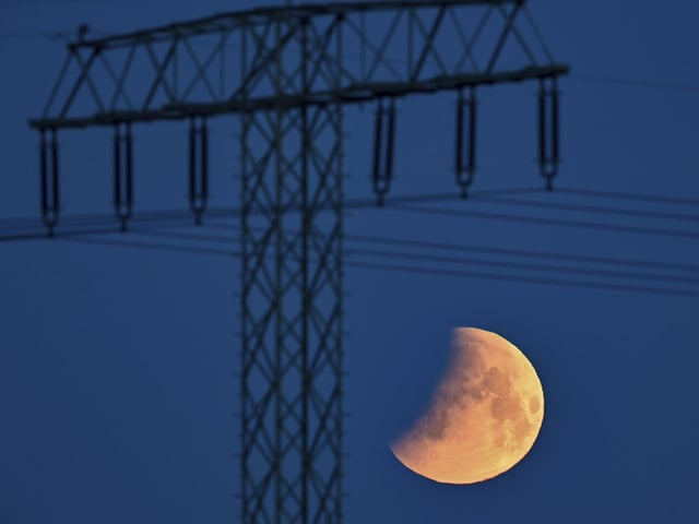 The beginning of the lunar eclipse is seen in the early morning next to a high voltage pylon in Jacobsdorf, Germany (Patrick Pleul/dpa via AP)
