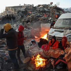 Survivors gather next to a bonfire outside collapsed buildings in Kahramanmaras on February 8, 2023, after their homes were destroyed in a 7.8 magnitude earthquake which struck the border region of Turkey and Syria on February 6. The sprawling scale of the disaster that flattened thousands of buildings, trapping an unknown number of people, has swamped relief operations already hampered by freezing weather. (Photo by Adem ALTAN / AFP) (Photo by ADEM ALTAN/AFP via Getty Images)