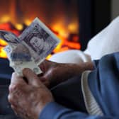 An elderly man holds cash in his hands as he warms himself in front of a fire. Picture: Matt Cardy/Getty Images