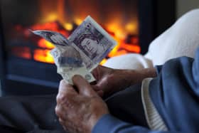 An elderly man holds cash in his hands as he warms himself in front of a fire. Picture: Matt Cardy/Getty Images