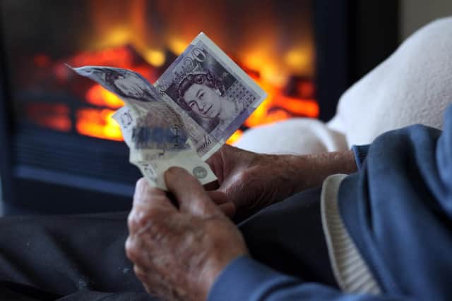 An elderly man holds cash in his hands as he warms himself in front of a fire. Picture: Matt Cardy/Getty Images