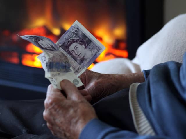 An elderly man holds cash in his hands as he warms himself in front of a fire. Picture: Matt Cardy/Getty Images