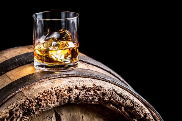 Glass of whisky with ice on old wooden barrel.