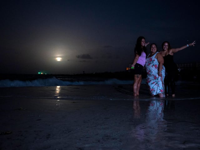 People pose for a picture as they gather to watch a full moon, the "Strawberry supermoon", as it rises in Miami Beach, Florida on June 14, 2022 (Photo by CHANDAN KHANNA/AFP via Getty Images)