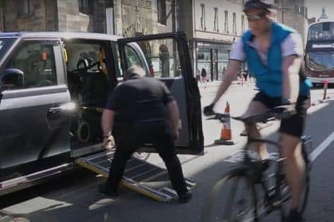 Cyclist in designated lane is close to taxi driver helping disabled passenger