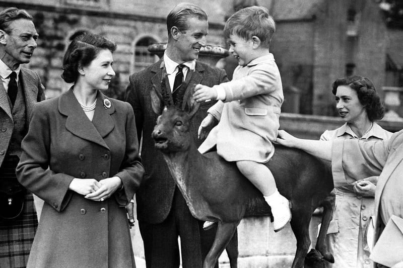 Prince Charles sitting on a statue watched by Princess Elizabeth, the Duke of Edinburgh, Princess Margaret and Queen Elizabeth while on holiday at Balmoral in August 1951.