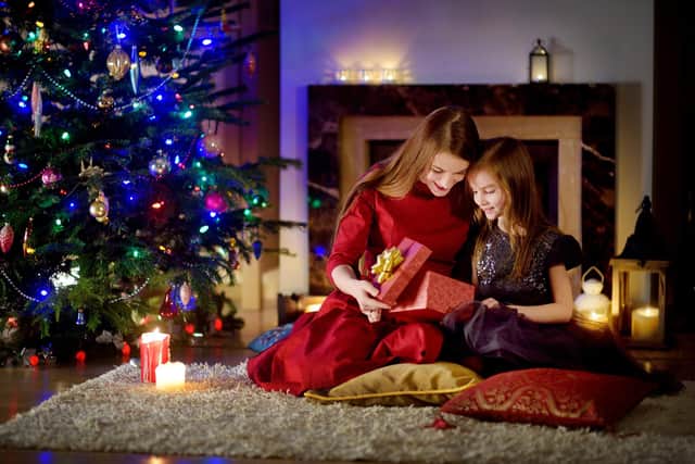 Young mother and her daughter unwrapping Christmas gifts by a fireplace in a cozy dark living room on Christmas eve