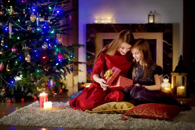 Young mother and her daughter unwrapping Christmas gifts by a fireplace in a cozy dark living room on Christmas eve