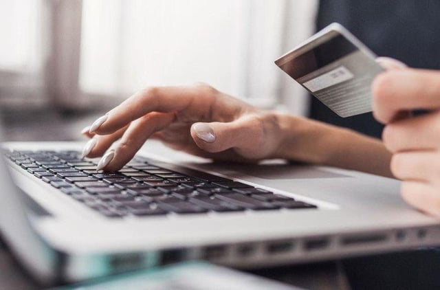 A stock image of a person at a computer with their bank card.
