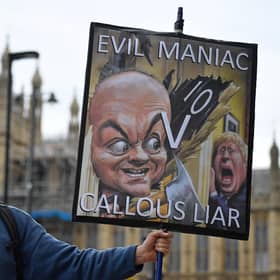 A demonstrator holds a placard showing Boris Johnson and his former special adviser Dominic Cummings outside the UK Parliament (Picture: Justin Tallis/AFP via Getty Images)