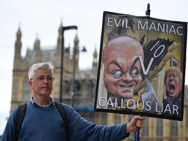 A demonstrator holds a placard showing Boris Johnson and his former special adviser Dominic Cummings outside the UK Parliament (Picture: Justin Tallis/AFP via Getty Images)