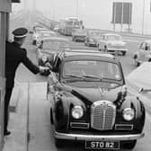 A driver pays the toll at the Forth Road Bridge in 1964, handing the money to a uniformed collector ... and how cars have changed too!
