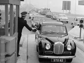 A driver pays the toll at the Forth Road Bridge in 1964, handing the money to a uniformed collector ... and how cars have changed too!