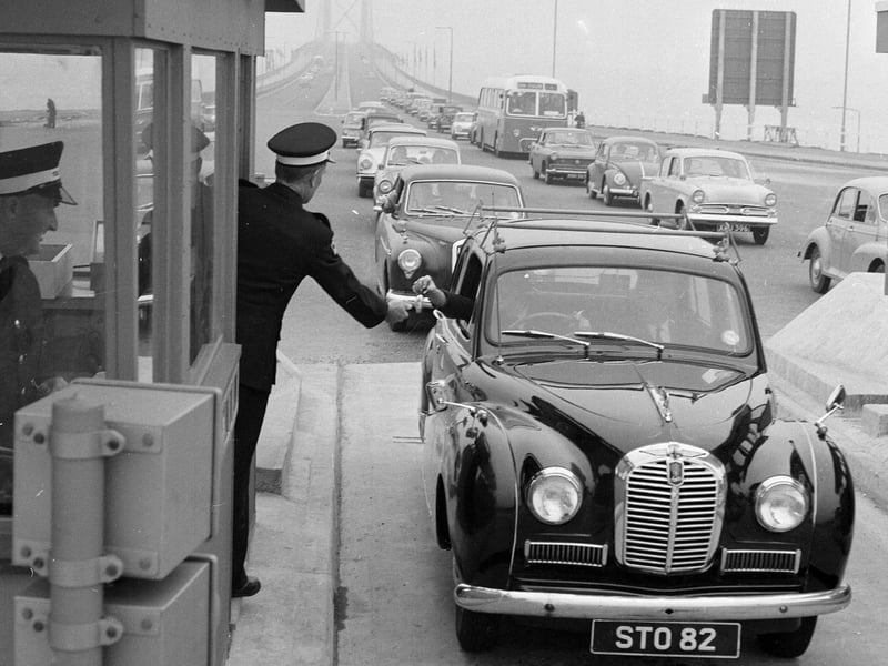 A driver pays the toll at the Forth Road Bridge in 1964, handing the money to a uniformed collector ... and how cars have changed too!